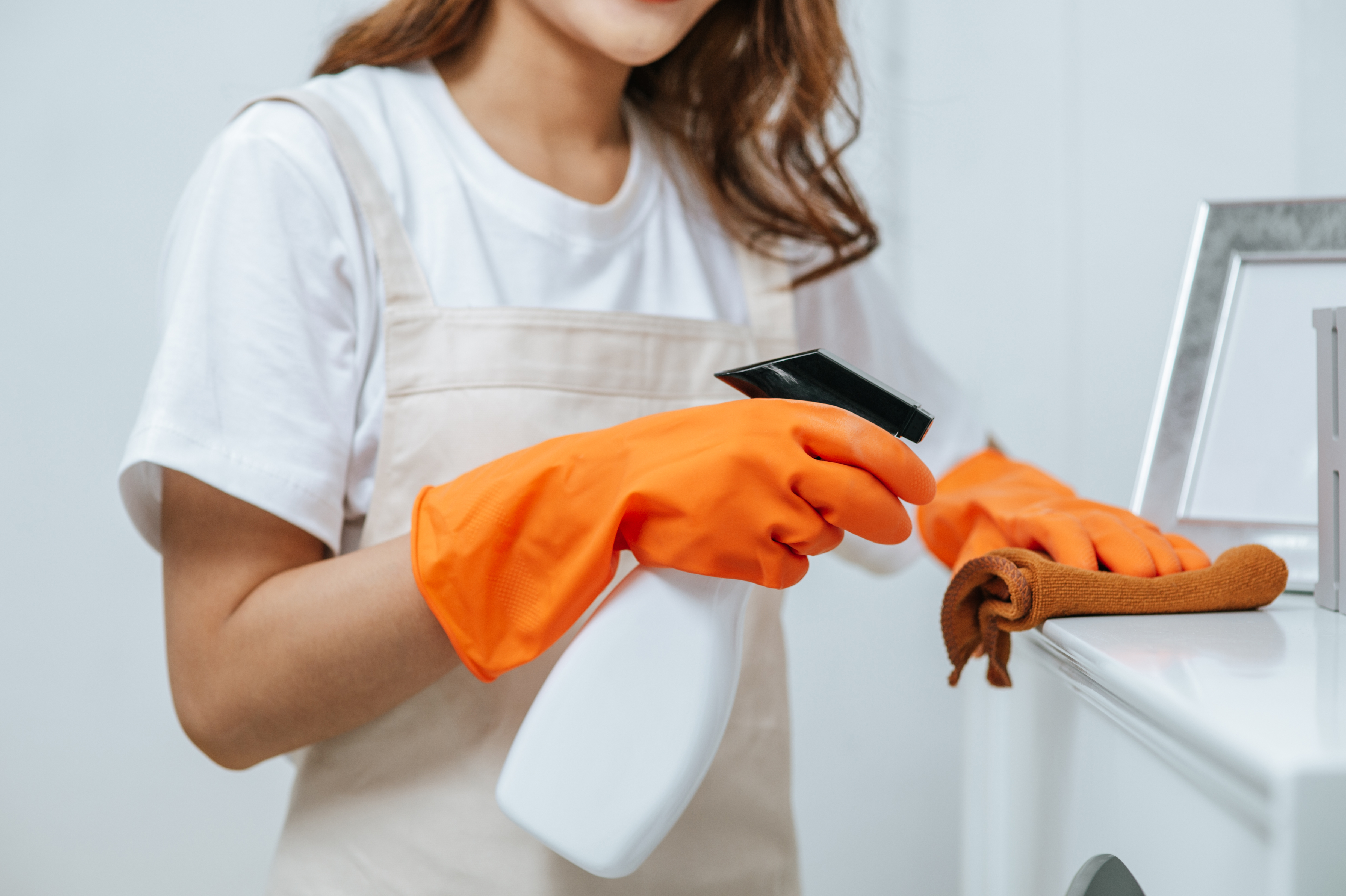 Close up hand young housekeeper woman rubber gloves use cleaning solution spray bottle white furniture use cloth clean it