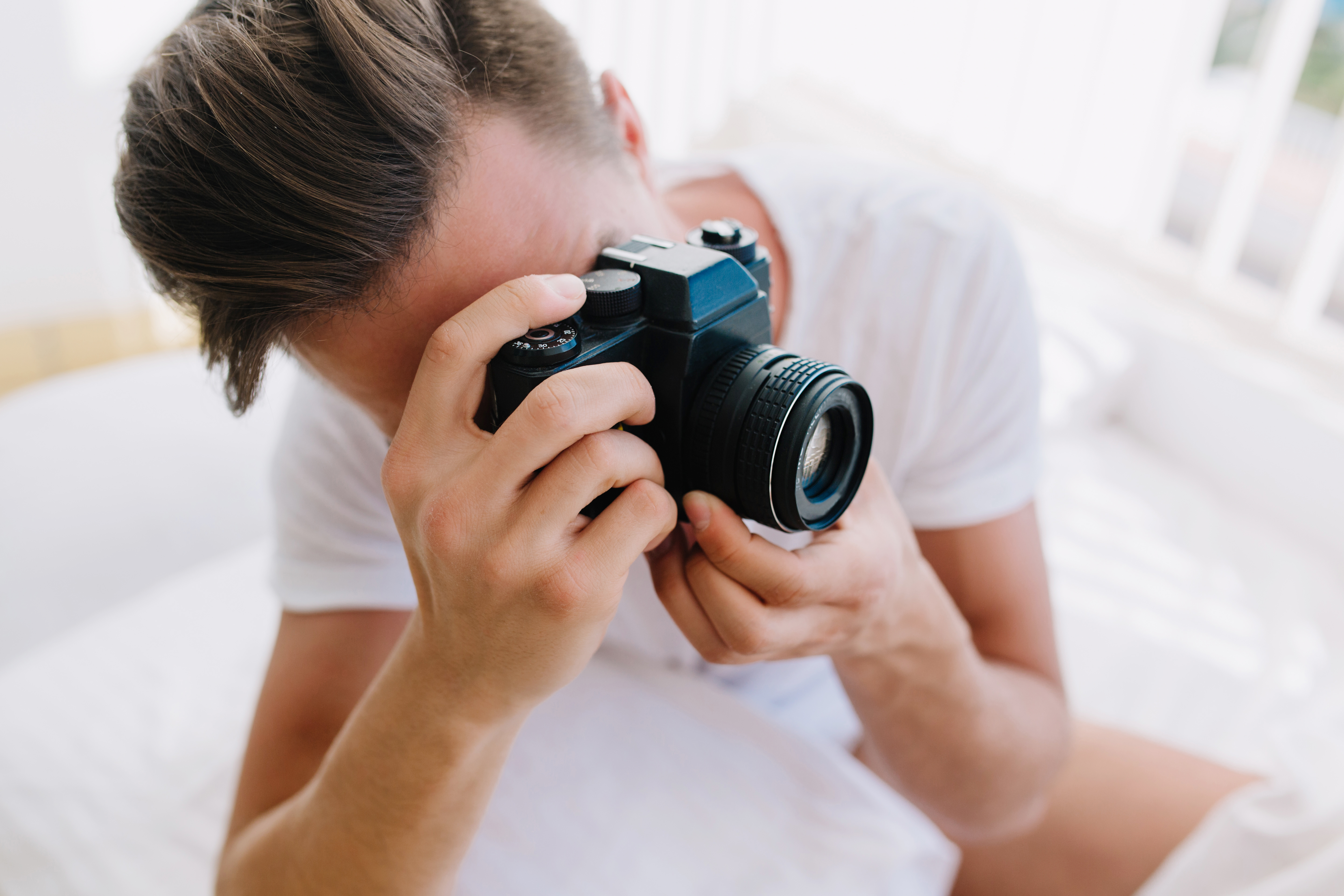 Close up portrait young man with trendy hairstyle holding professional camera hands guy with dark short hair white shirt making new photos portfolio sunny morning